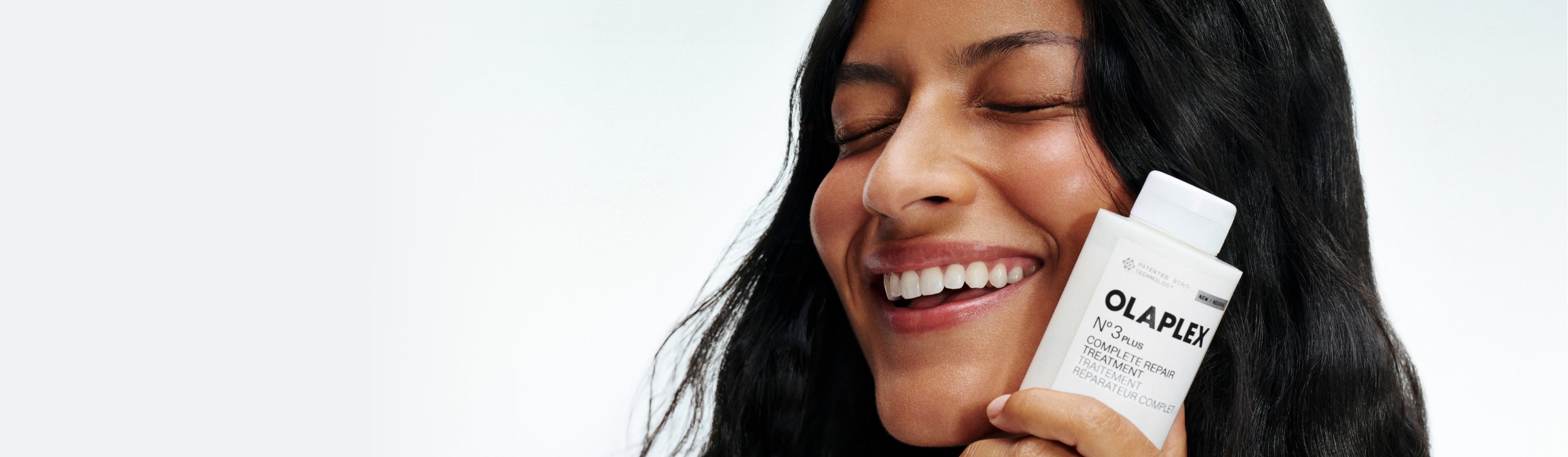 Woman smiling while holding No.3PLUS bottle close to her face 