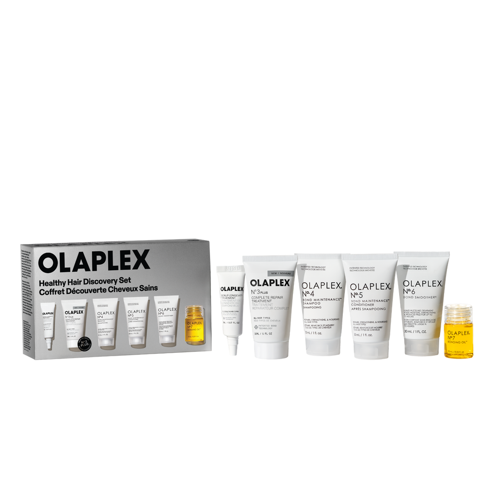 A retail packshot of the Olaplex Healthy Hair Discovery Set against a transparent checkerboard background. On the left is the product box, and arranged to the right are five white travel-size tubes (No. 3, No. 4, No. 5, No. 6, and a smaller tube) alongside a small clear bottle of No. 7 Bonding Oil filled with yellow liquid. - main view