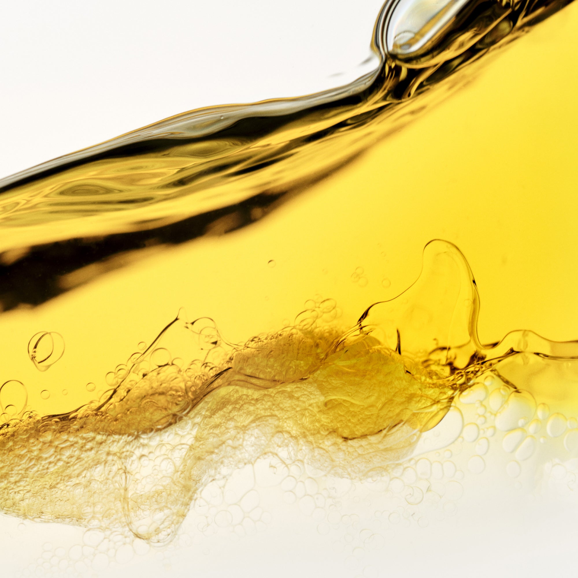 hover

A vibrant close-up macro abstract of a golden-yellow oil or serum liquid, creating dynamic waves and swirling textures against a crisp white background. Tiny, delicate bubbles are scattered throughout the translucent fluid, capturing the light.
